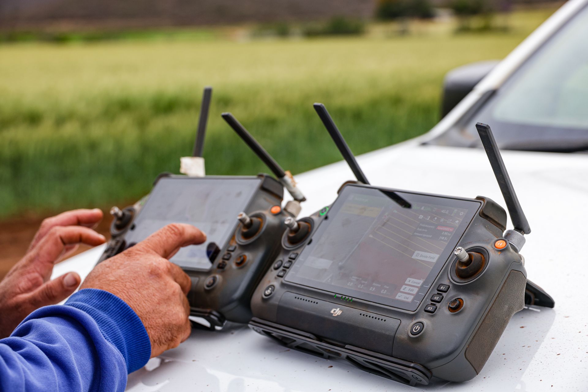 Farmers operating drone controllers over a green field