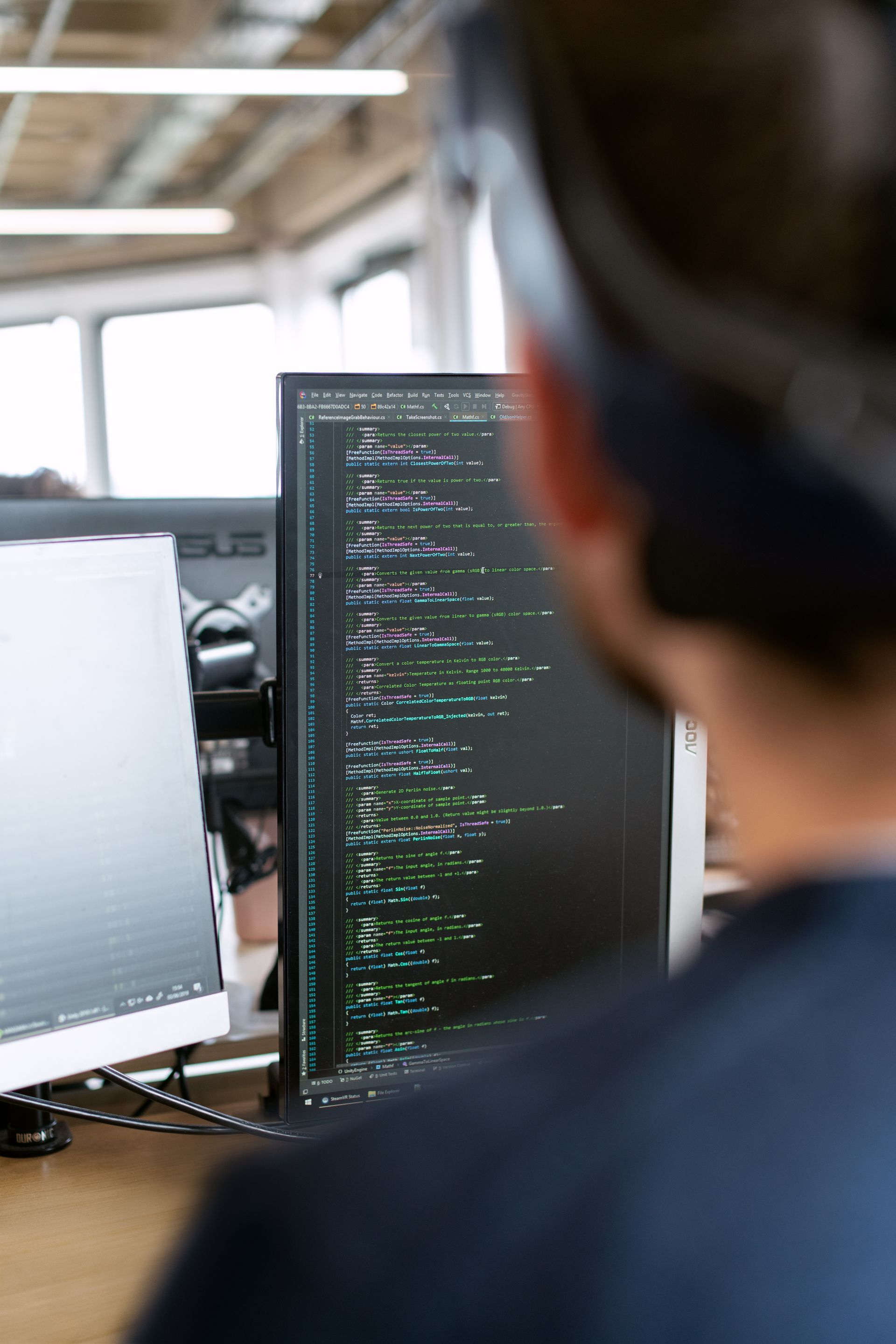 A software engineer studying code across two monitors in a modern office