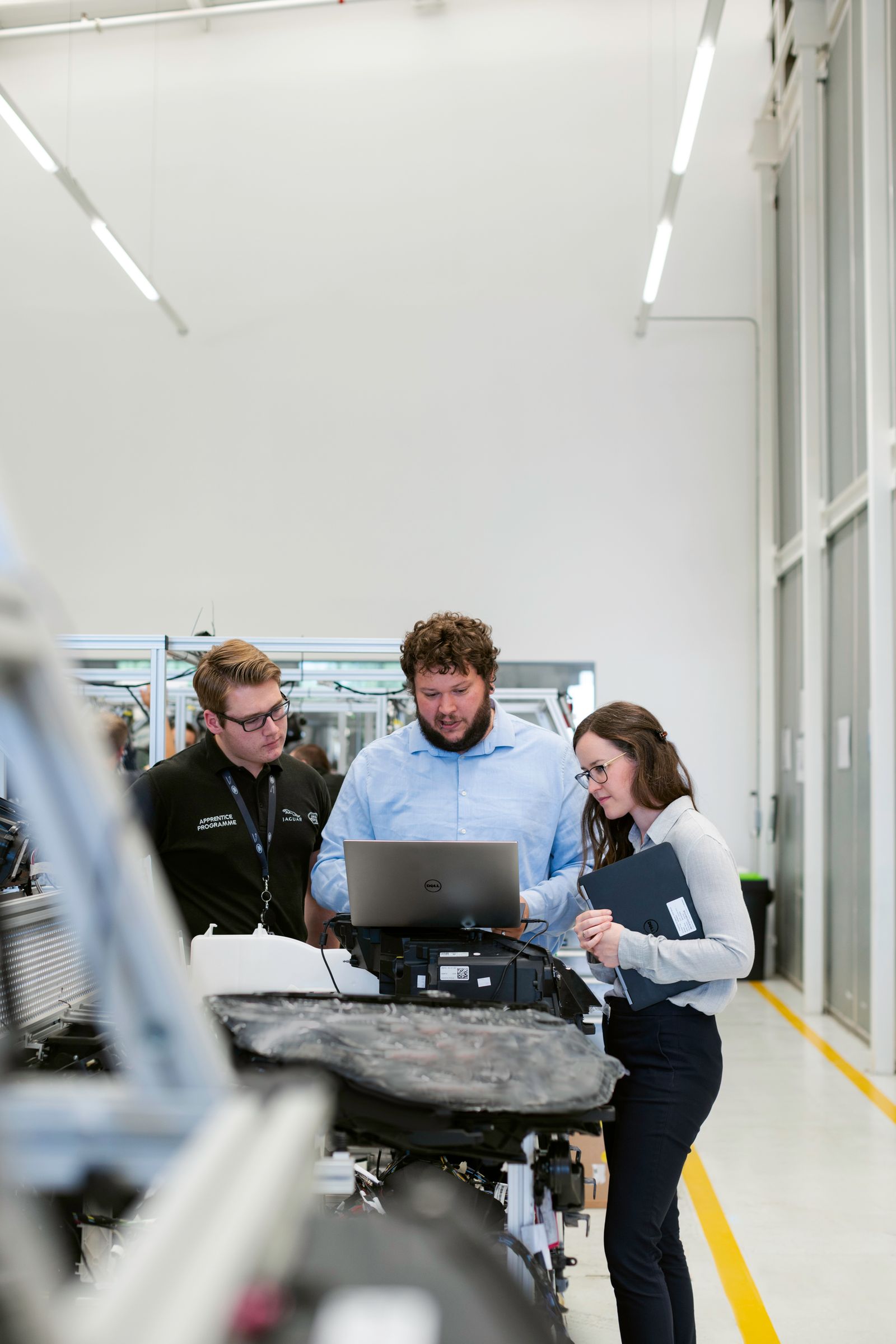 Three engineers building capability around a laptop in a bright facility