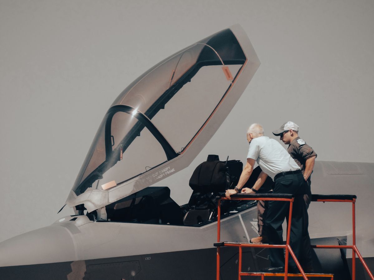 Two technicians inspecting a military aircraft cockpit on a clear day